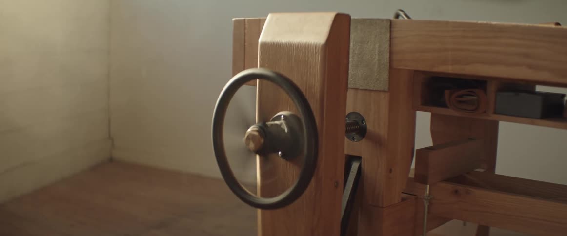 A man spinning a wheel closing a vice on a workbench