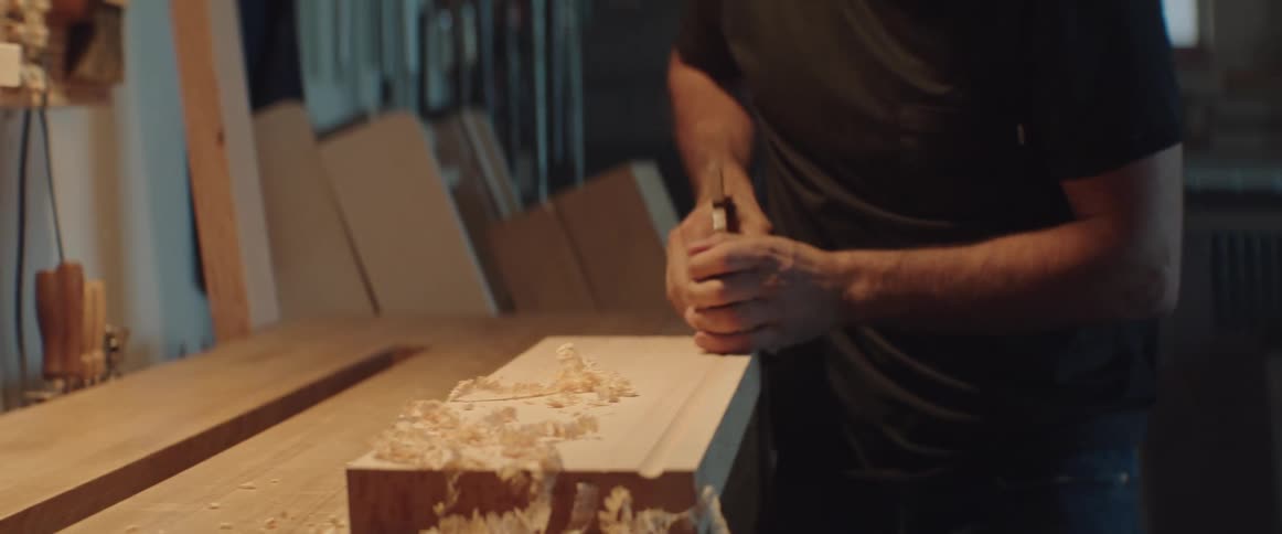 A man uses a tool to carve grooves into a piece of wood at night