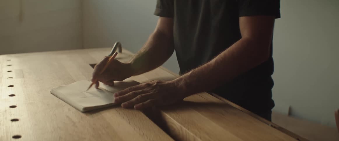 A man sketching in a book on a workbench