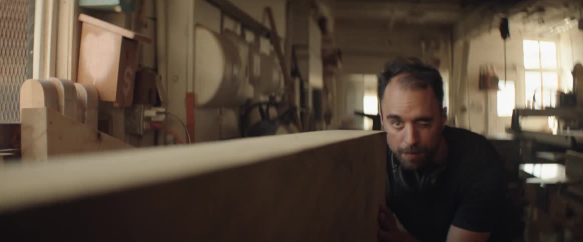 A man moves and examines a large piece of lumber in a workshop