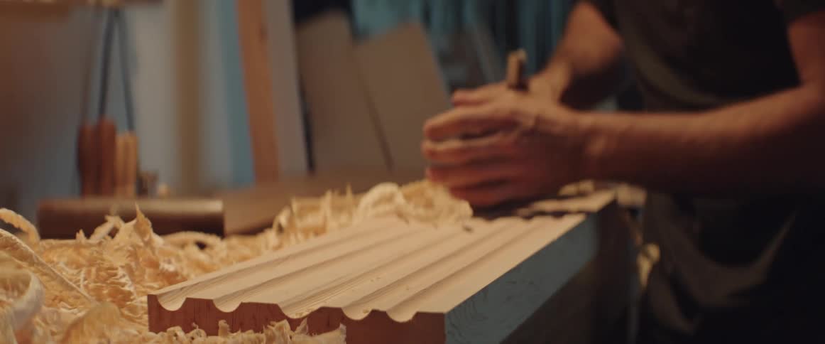 Carpenter uses a hand plane inside a workshop to shave thin layers of wood from a plank