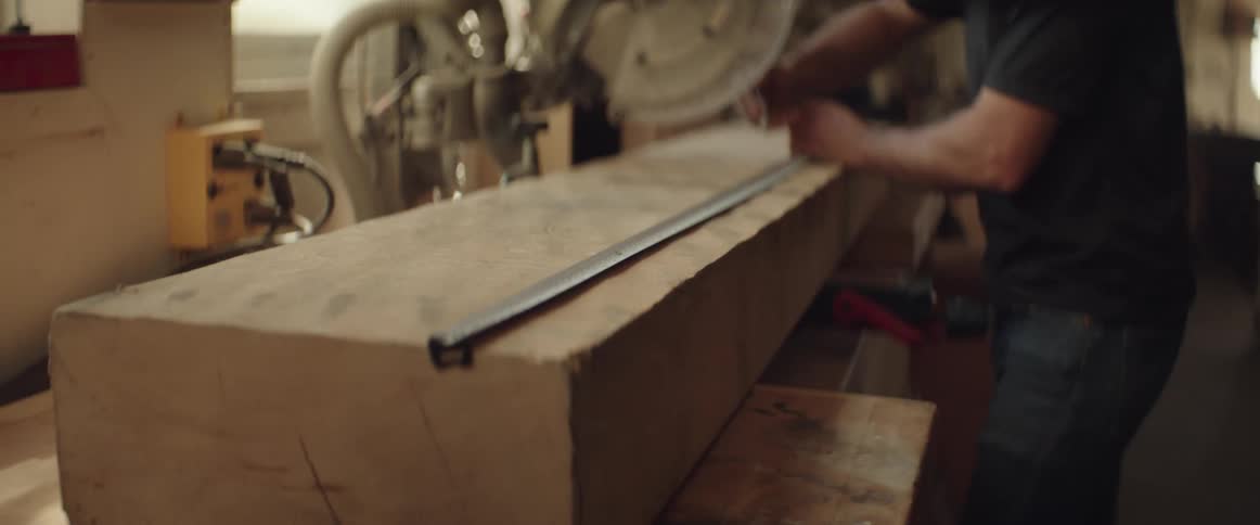 Male woodworker measures long block of wood in workshop