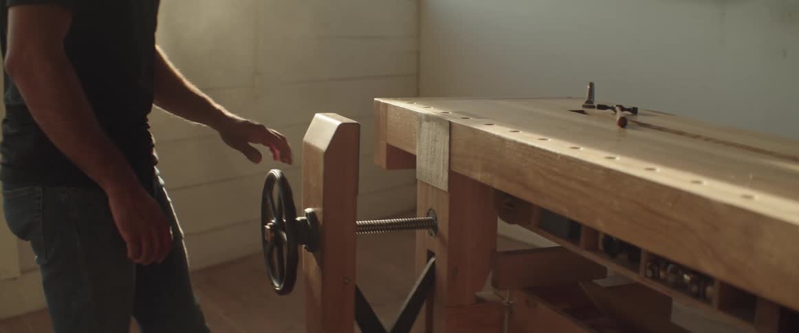 A man is spinning the wheel on a vice on a workbench