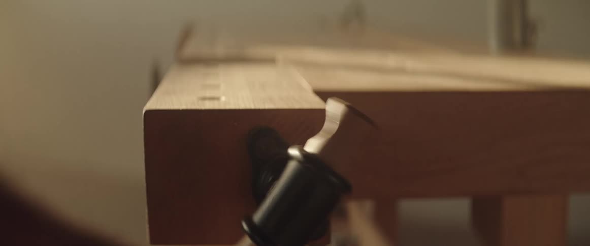 A carpenter is spinning the handle on a vice on his work bench