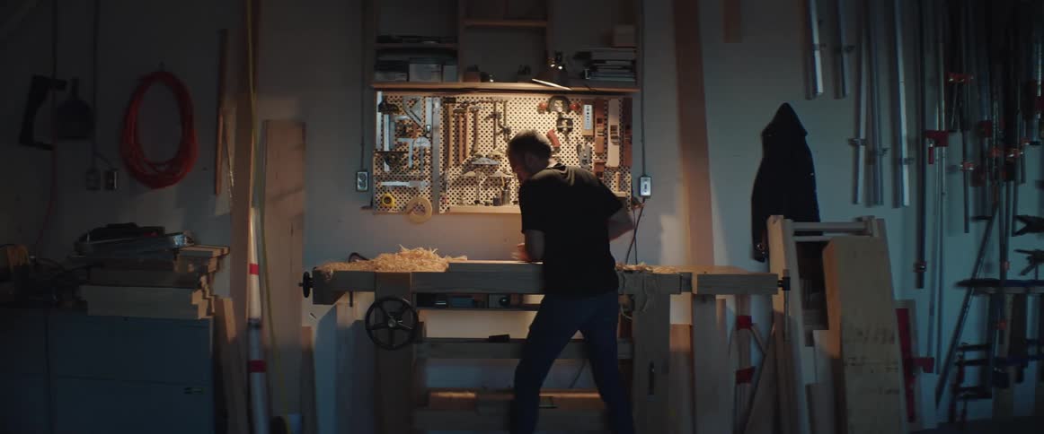A man is using a planer on wood in a workshop at night