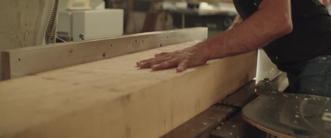 A man in a shop pushes a large piece of wood through a planer