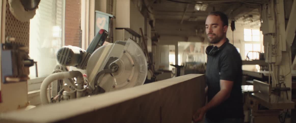 Carpenter places a large wooden plank onto a workbench inside a shop