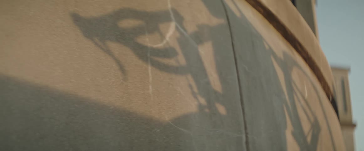 Shadow of cyclist carrying a bicycle flows across the concrete wall of a building