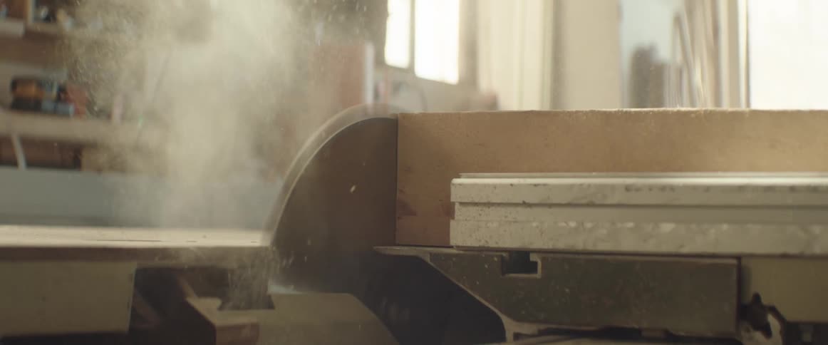 Man uses a circular saw to trim the side of a wooden board on a workshop
