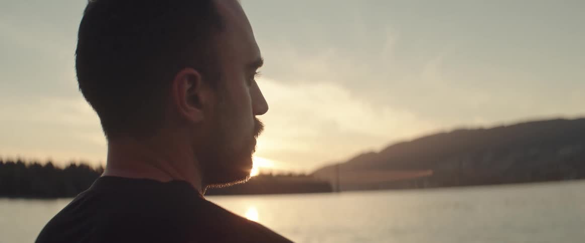 Man standing next to a lake contemplating the view ahead at sunset