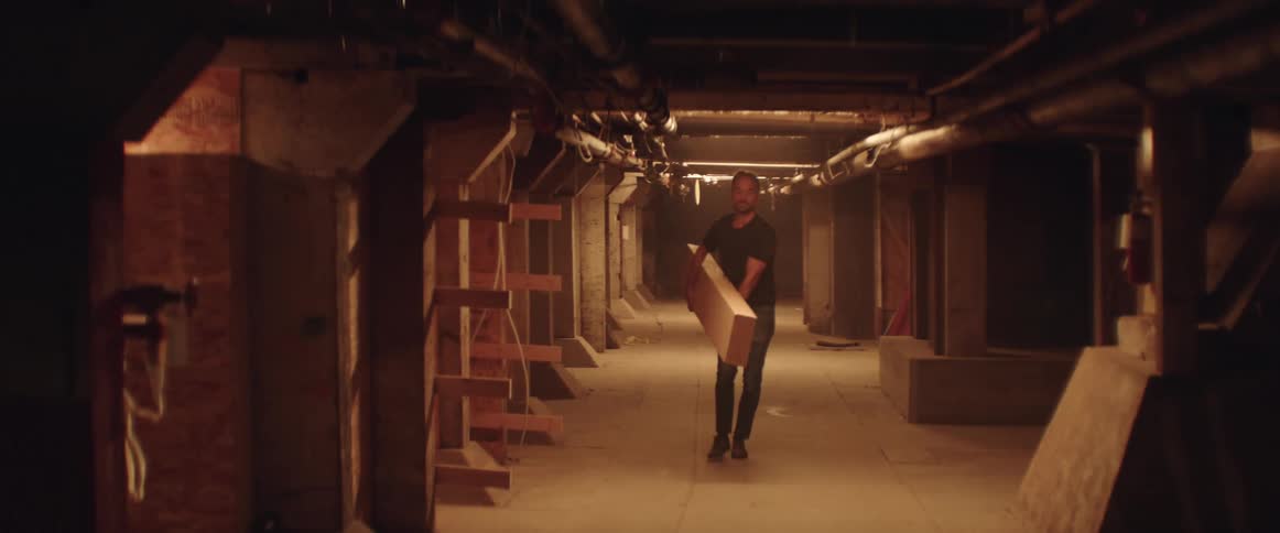 A man is carrying a large piece of lumber down an industrial corridor