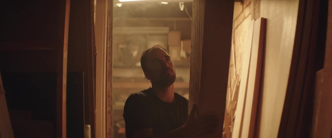 A man chooses a piece of lumber from his store room and carries it down the hall
