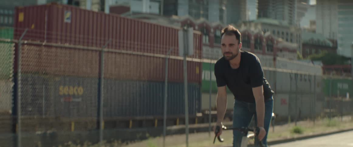 Man riding a bicycle in an empty street in a big city near some shipping containers