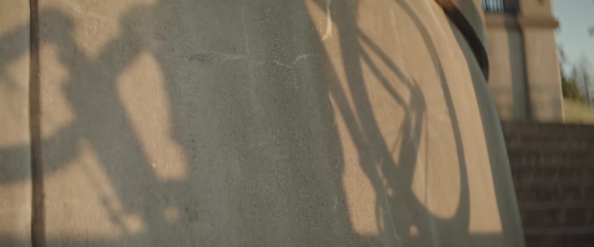 Shadow of a person passing by carrying a bicycle against a stone wall at sunset