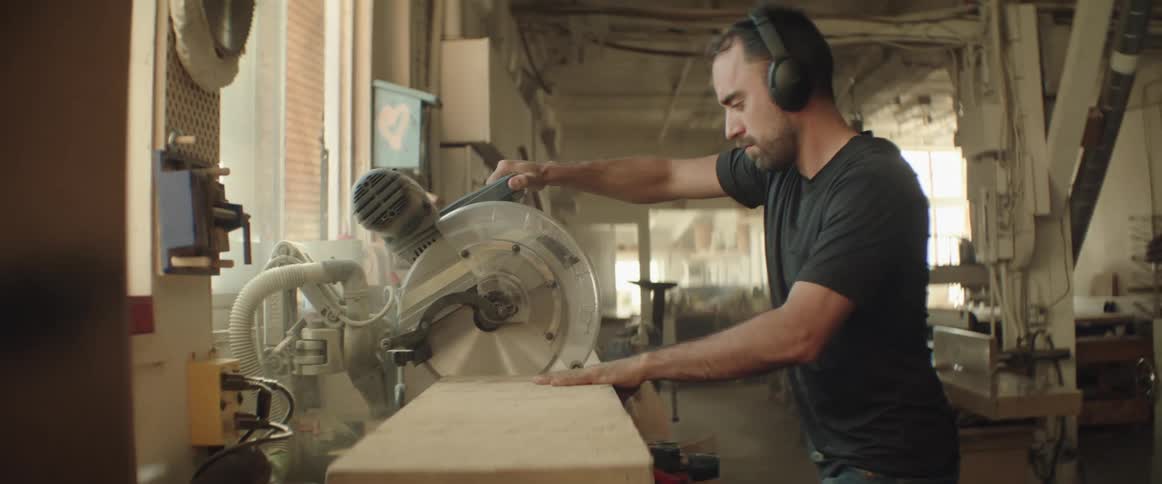 A man uses a standing circular saw to cut through a thick plank of wood