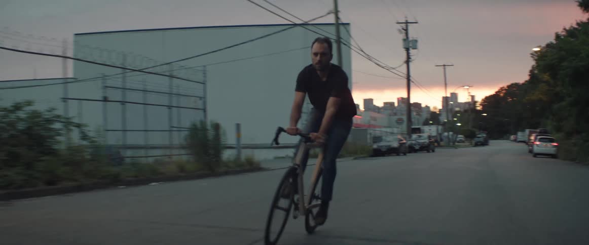 Man with beard and black t shirt rides bicycle on road at sunset