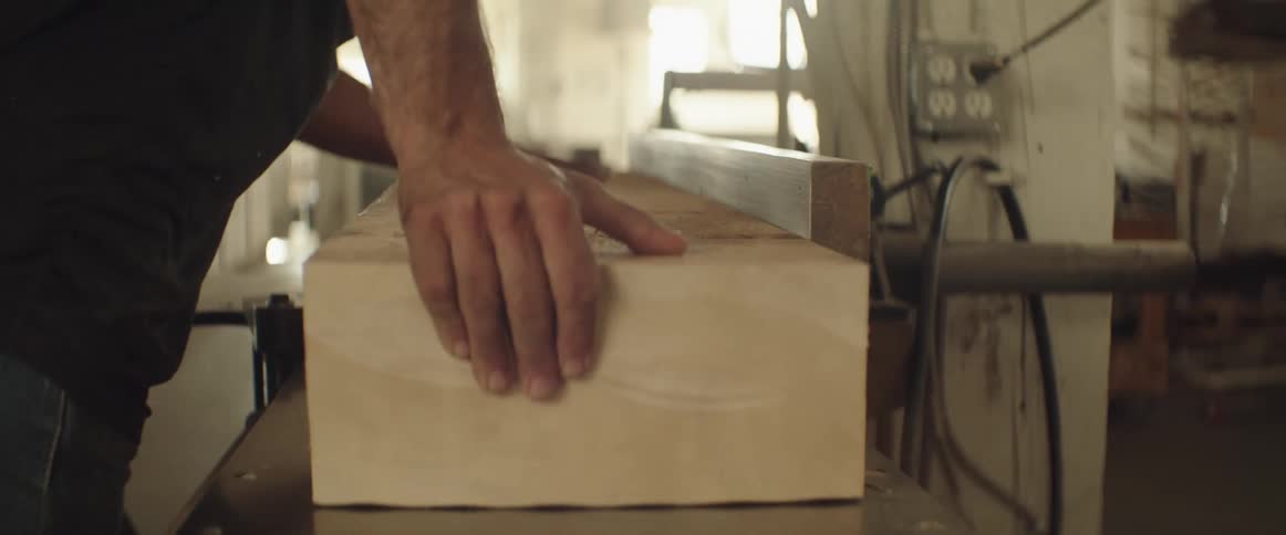 A carpenter pushes a large piece of wood across a planer