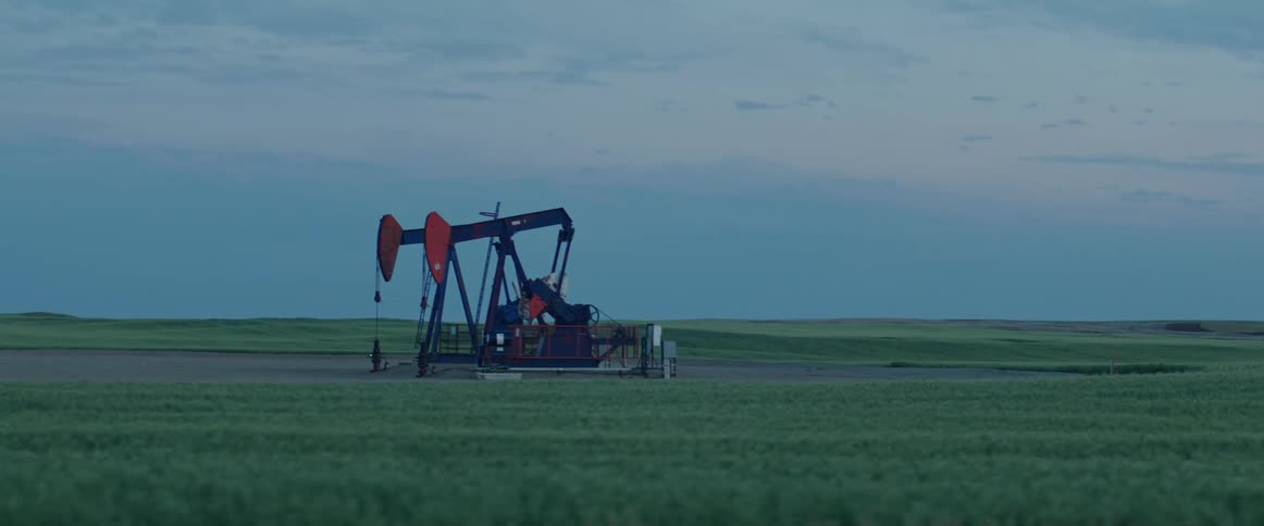 Two oil pumpjacks near fields of green grass under evening sky