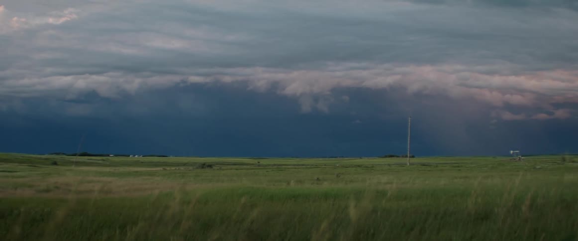 Grass moves in the breeze as storm clouds roll in and lightning flashes in the sky