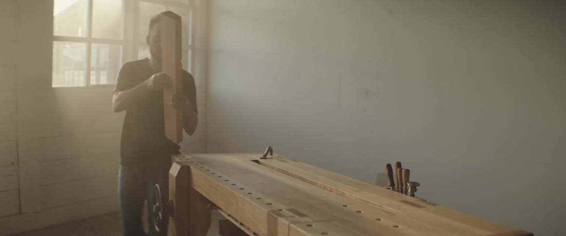 Carpenter places a piece of wood on a vice attached to a workbench in his workshop