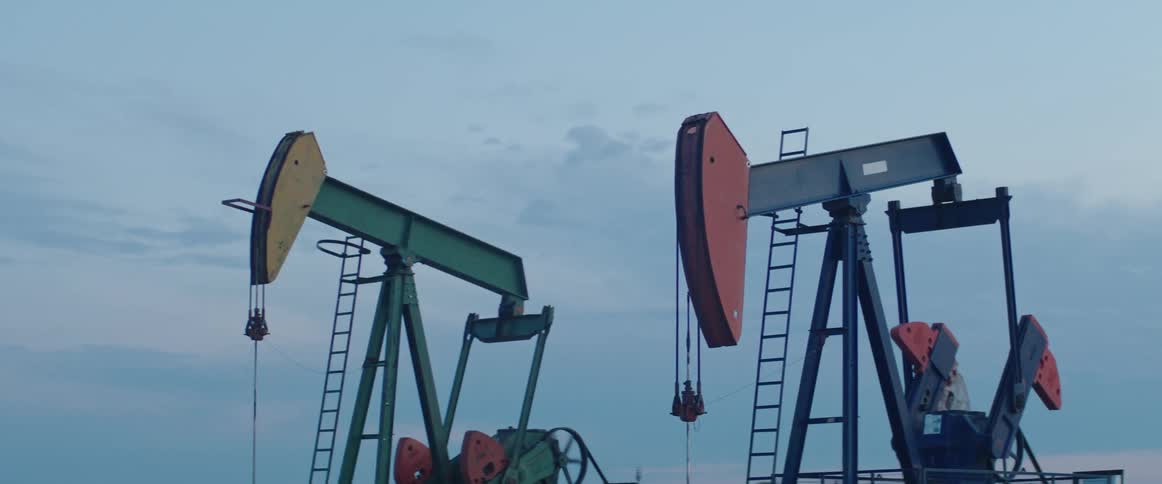 Oil pumps working on a field in the countryside at evening seen from a moving camera