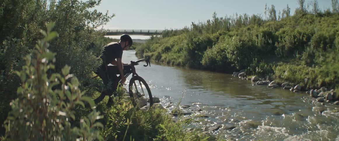 Man carrying his gravel bike to the edge of a river on a sunny day