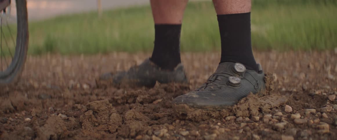 A mans feet are in the mud next to a bicycle tire
