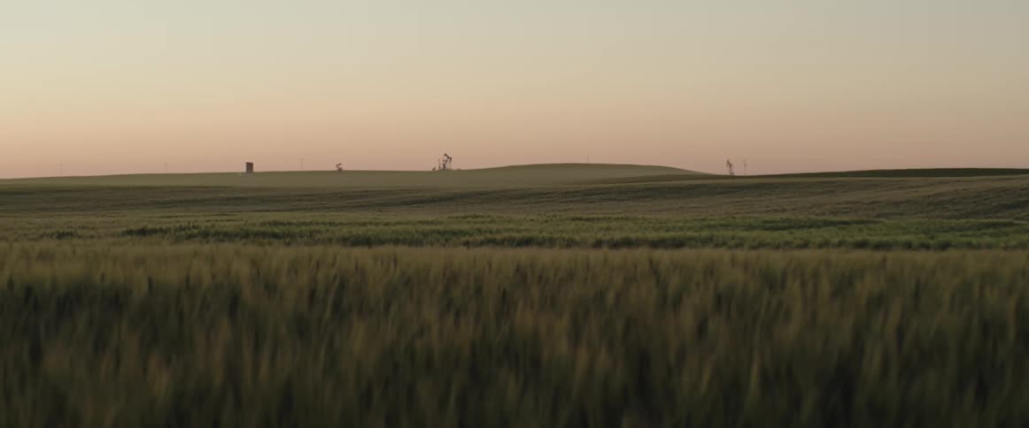 Green grassland hills with distant pump jacks during sunset