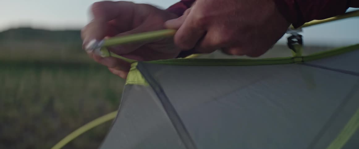Close up of the hands of a man assembling a tent in the countryside at evening