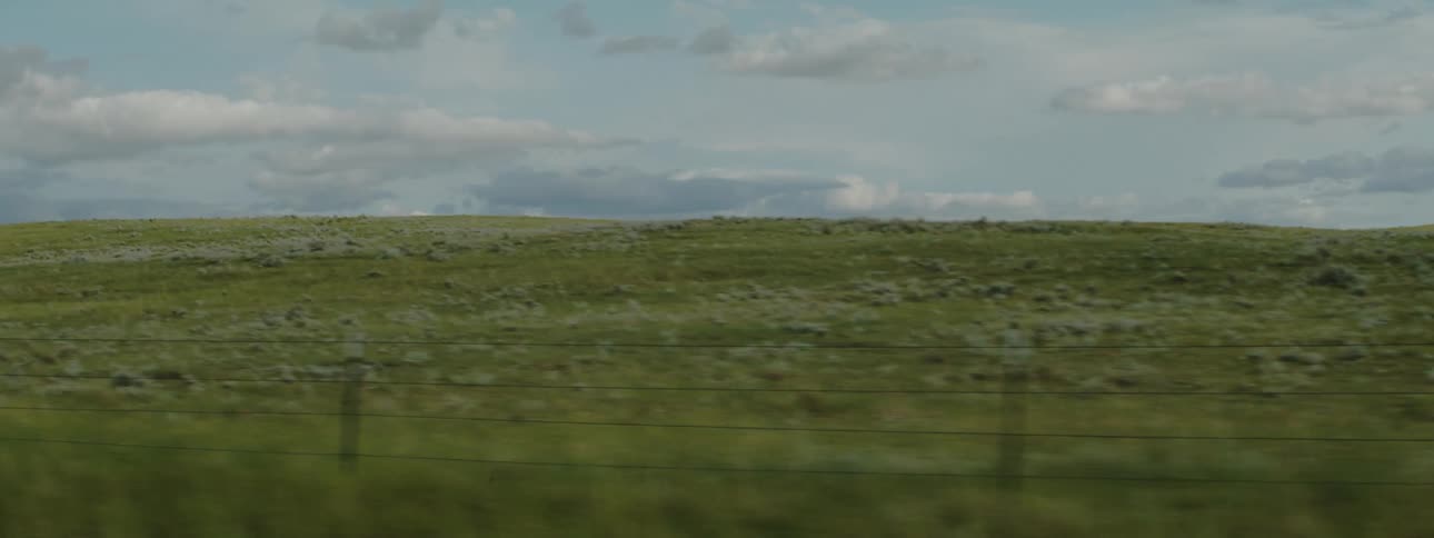 A sprawling grassy field is lined with a simple barbed wire fence