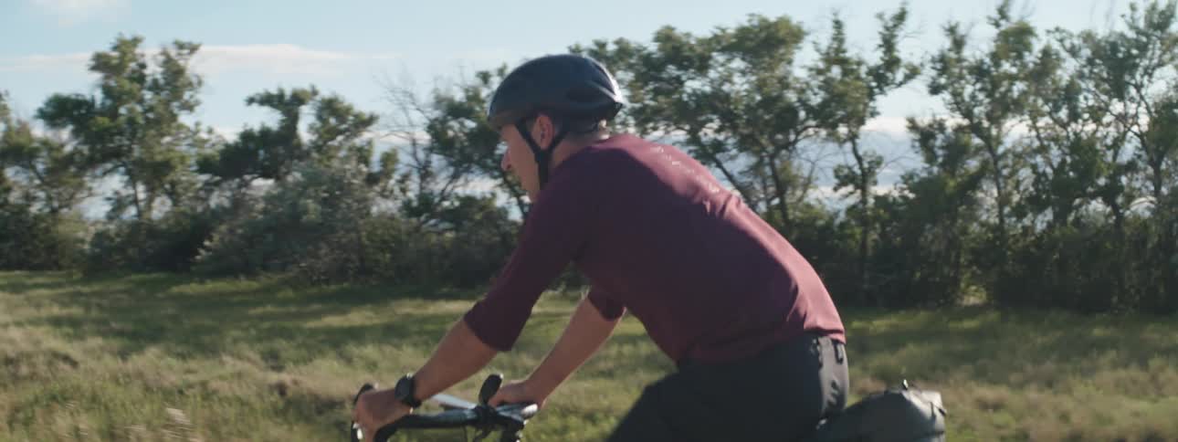 Road cyclist wearing a helmet rides on a rural road in the daytime under a blue sky