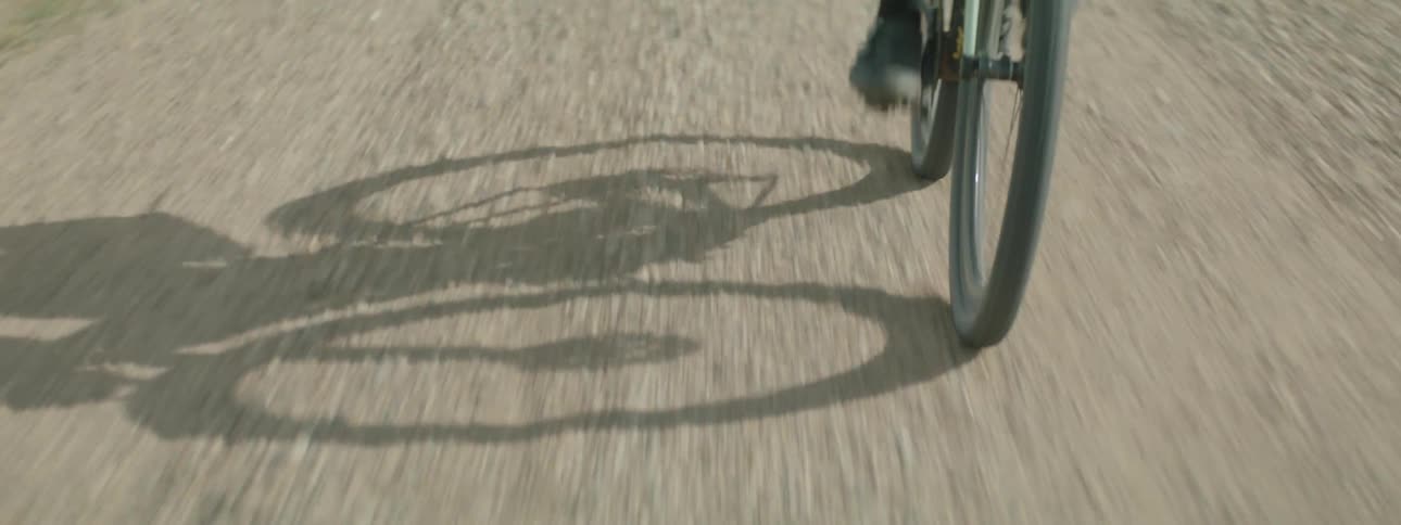 A person's shadow seen riding a bicycle down a gravel road
