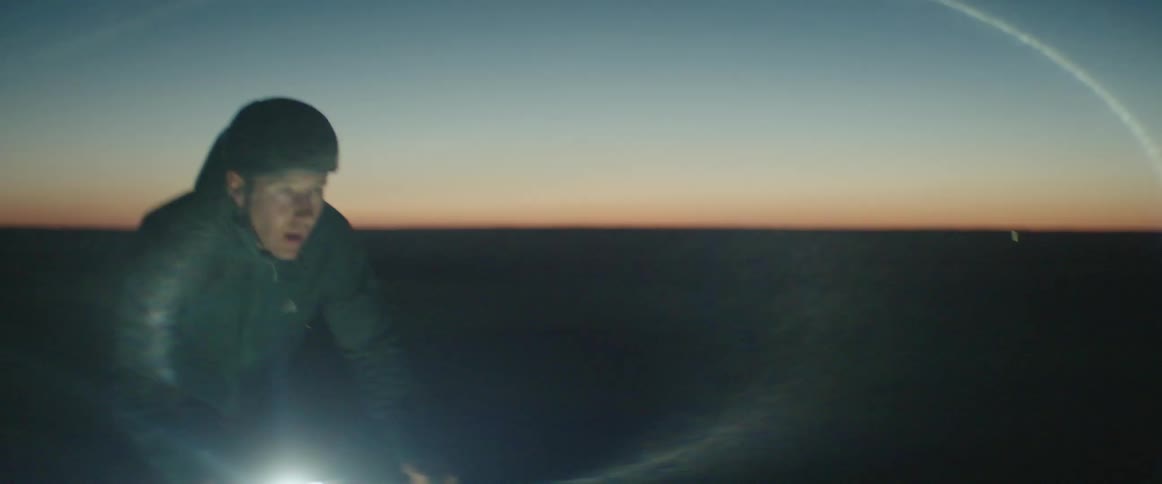 Man wearing a safety helmet riding a bike in an open field at night