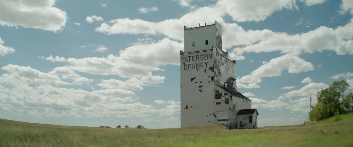 A dilapidated grain elevator sits in an open field during the day