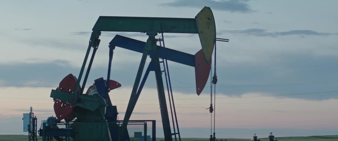Pump jacks move up and down in an oilfield at dusk