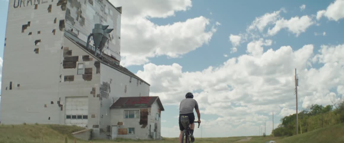 Man rides a bicycle near an abandoned building in the countryside