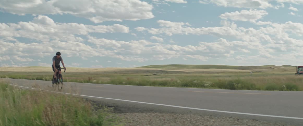 Male cyclist with black helmet shirt and shorts rides bicycle on highway between fields