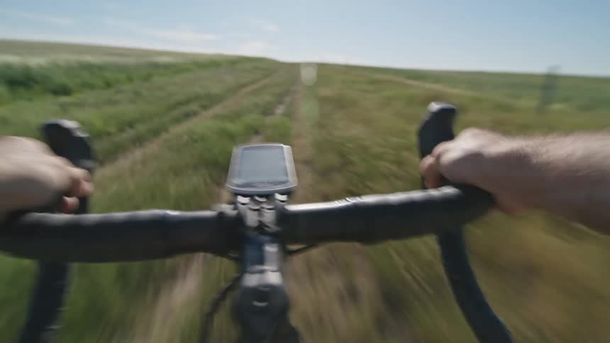 Point of view of man riding a bike on a path in the middle of a grass field at a sunny day
