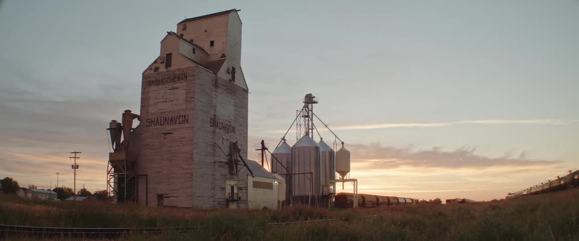 Train sits on tracks near silos and grain tower under a red tinted horizon