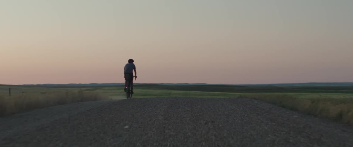 Man riding his bike in an empty road with hills in the background during sunset