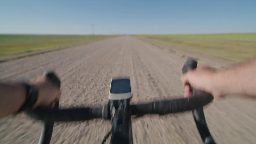 A first person view shows a bicyclist pedaling swiftly along a remote dirt road