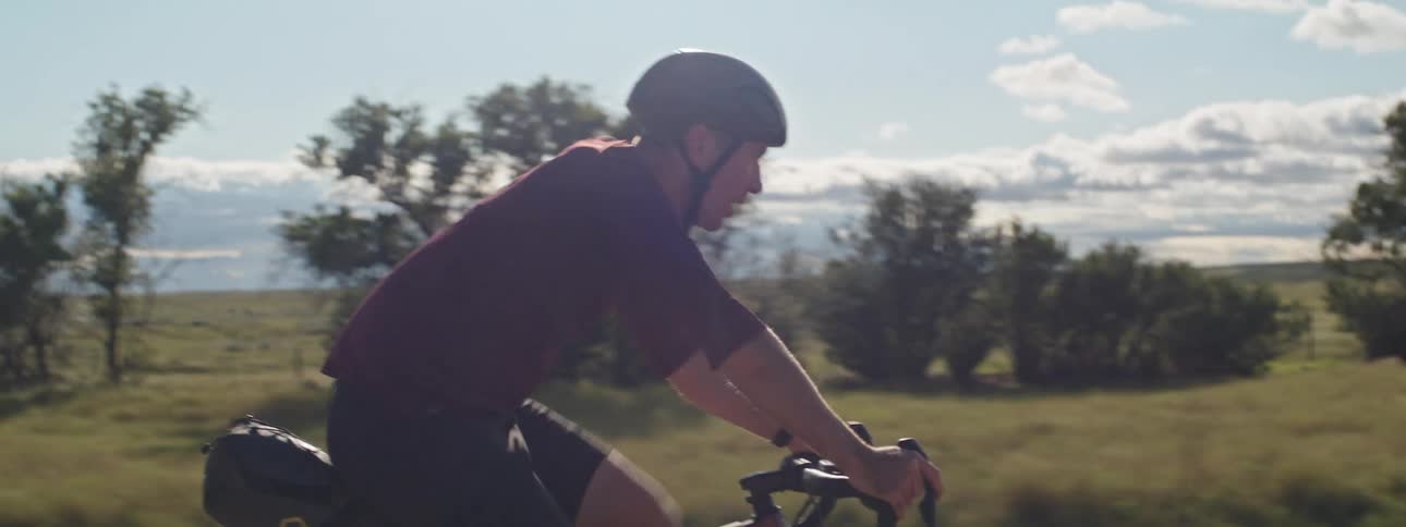 A man wearing a helmet is riding a bicycle on a rural road as the sun shines brightly upon him