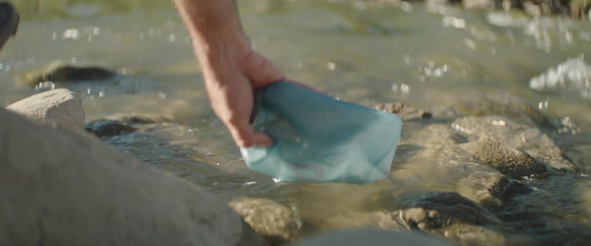 A man submerges water filter bag into a swiftly flowing stream