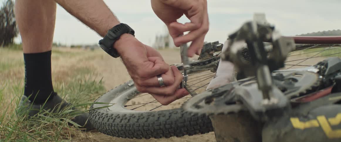 Man uses tools to fix the chain on a bicycle laying at the side of the road on a rural area