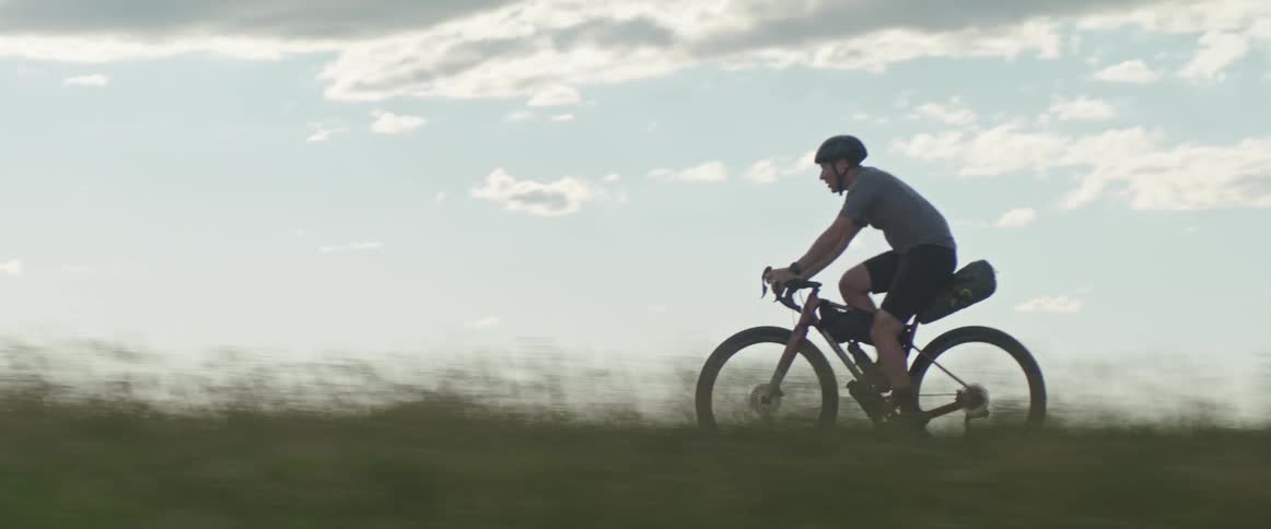 Male cyclist with helmet shirt and shorts pedals on country road against the sky in the countryside