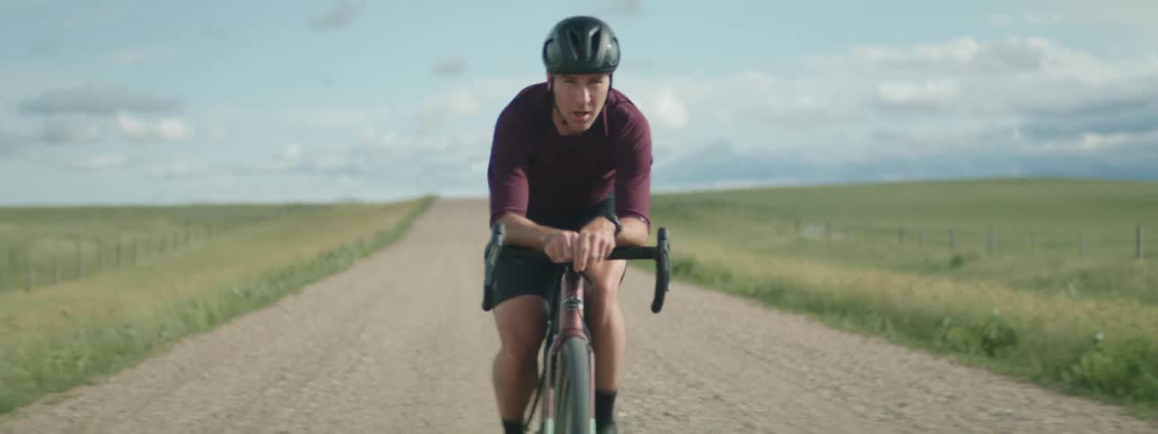 A man wearing a helmet is riding a bicycle on a wide open rural dirt road
