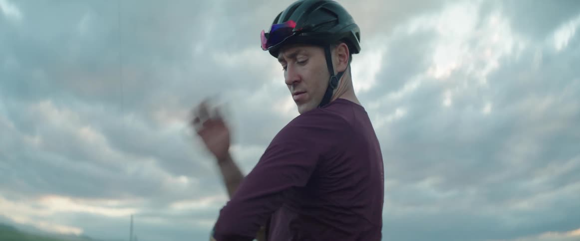 Male cyclist with helmet and red jersey dusts off his shoulders on country road in the evening