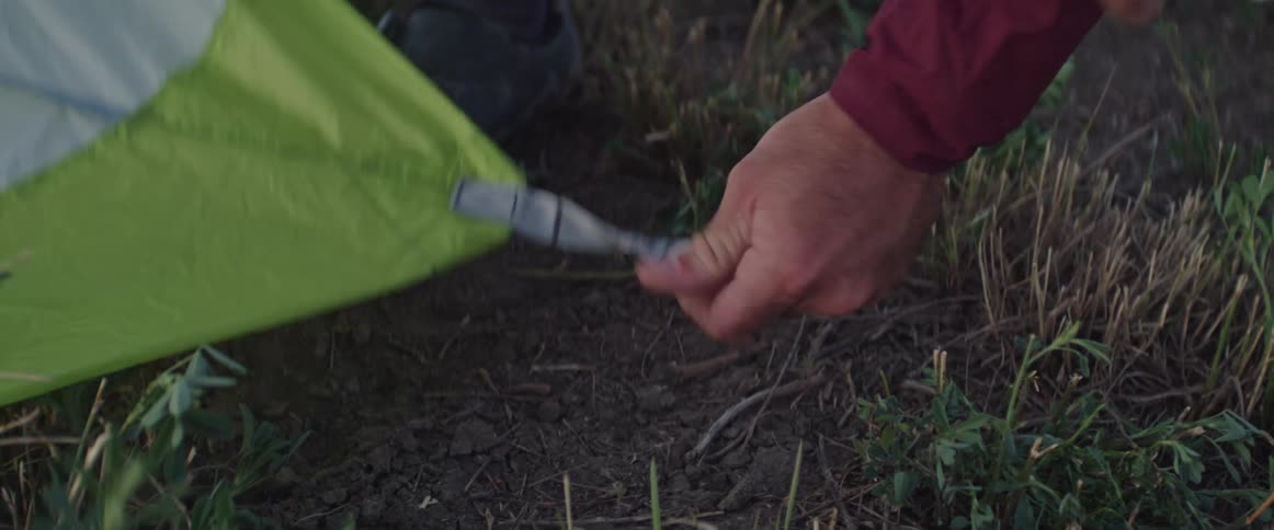 Man pins the sides of a tent on the ground while camping in the countryside