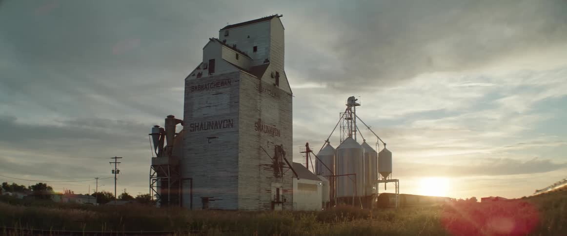 The sun is coming up over an old grain elevator and silos