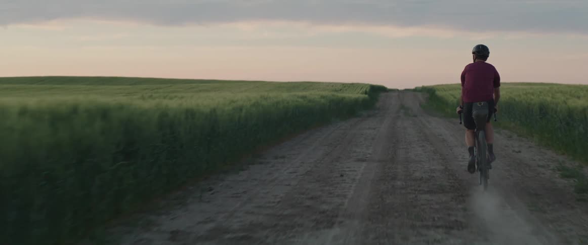 Man wearing a bike helmet riding his bicycle through a dirt road at sunset